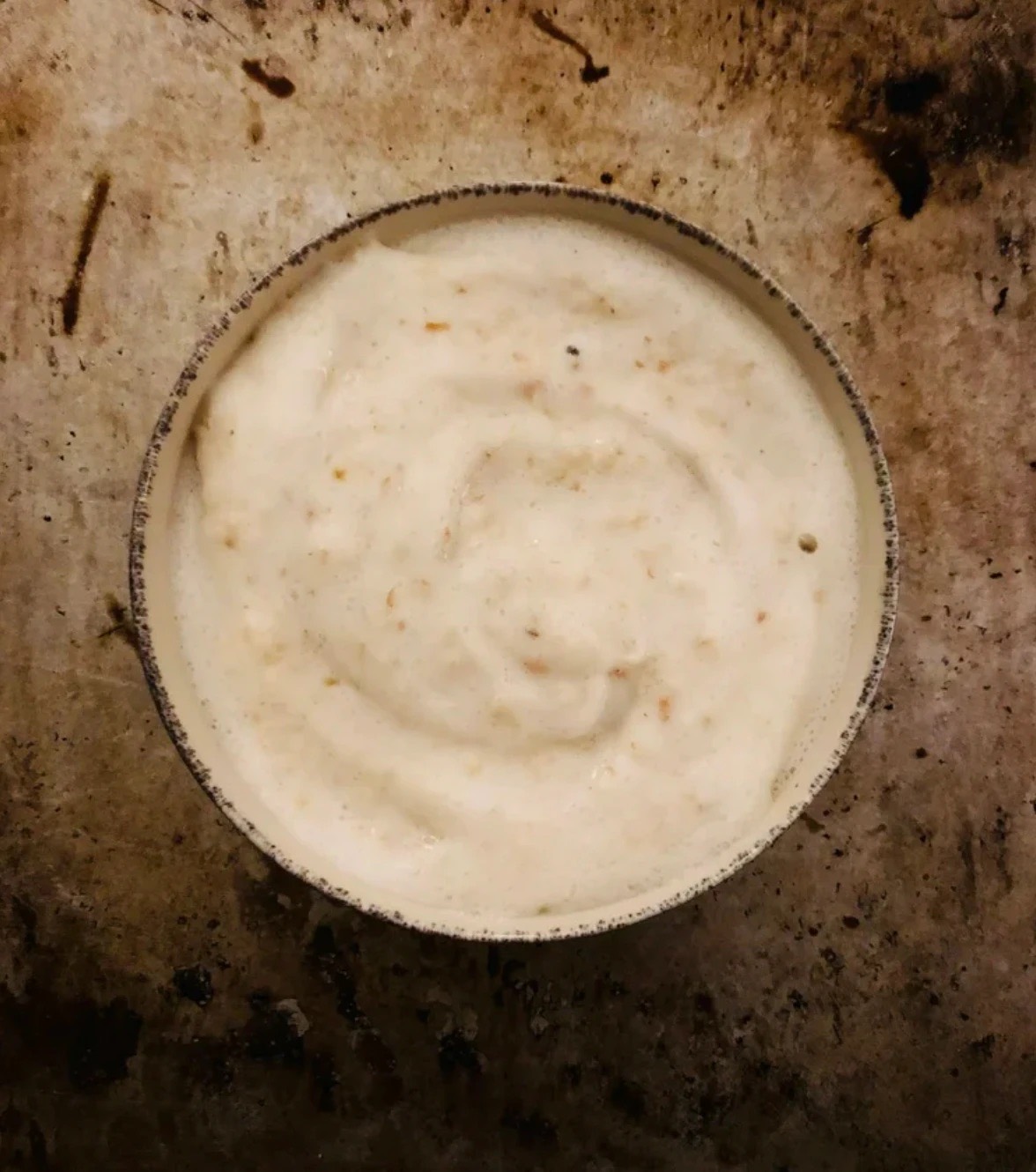 A bowl of creamed barley, pale and softly swirled, on a dark weathered pan